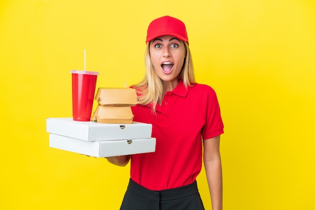 Delivery Uruguayan woman holding fast food isolated on yellow background with surprise facial expression