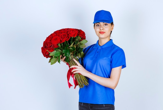 Delivery woman employee in blue uniform standing and holding bouquet of roses .