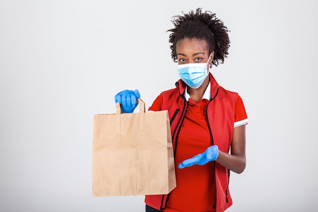 Delivery woman employee in red t-shirt uniform mask glove hold craft paper bag with food 