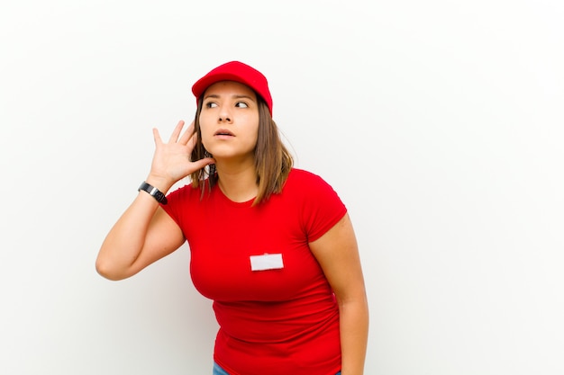 Delivery woman looking serious and curious, listening, trying to hear a secret conversation or gossip, eavesdropping against white background