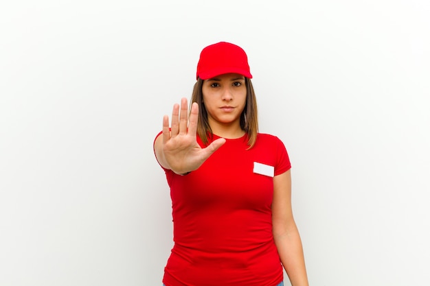 Delivery woman looking serious, stern, displeased and angry showing open palm making stop gesture against white 