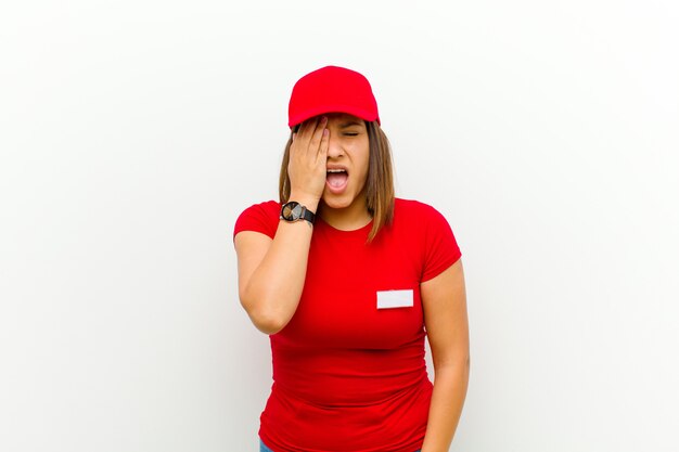 Delivery woman looking sleepy, bored and yawning, with a headache and one hand covering half the face