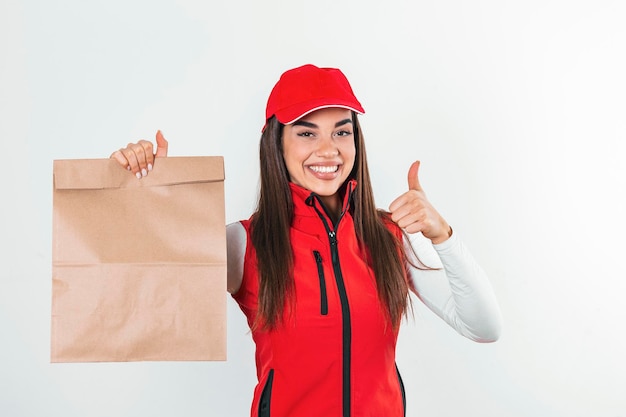 Delivery woman in red uniform hold craft paper packet with food isolated on white background studio portrait Female employee in cap tshirt print working as courier Service concept Mock up copy space