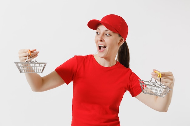 Delivery woman in red uniform isolated on white background. Female courier or dealer in cap, t-shirt, jeans holding metal grocery basket for shopping in supermarket. Copy space for advertisement.