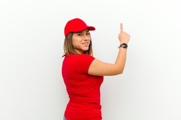 Delivery woman standing and pointing to object on copyspace, rear view against white 