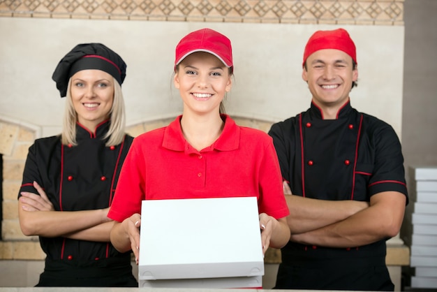 Delivery woman with boxes of pizza and two happy chef.