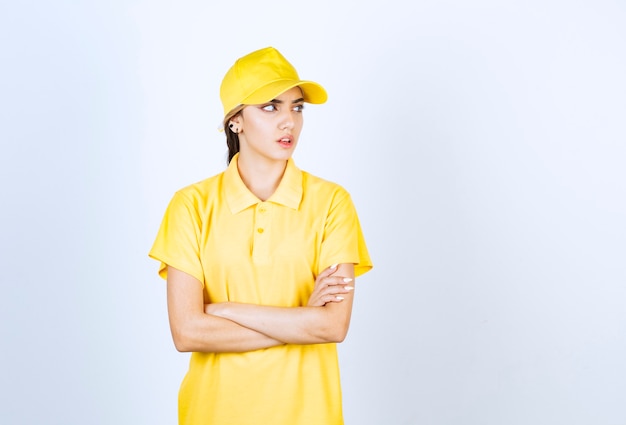 Photo delivery woman in yellow uniform standing and looking away against white wall.