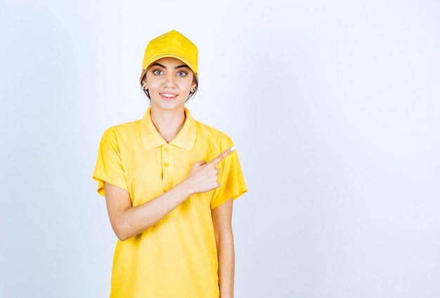 Donna delle consegne in uniforme gialla in piedi e che indica via con un dito indice.
