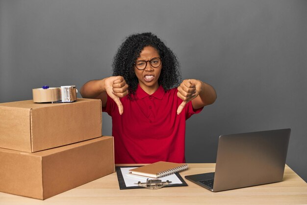 Foto delivery zakenvrouw met inventaris en dozen met duim naar beneden en uitdrukking van afkeer