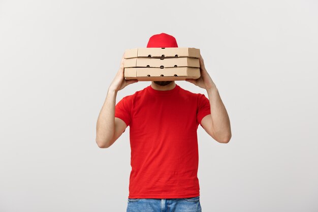 A Deliveryman hidden behind a large stack of pizza boxes he is carrying. Isolated over grey