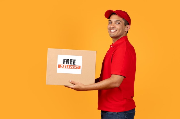 Deliveryman holds cardboard box with free delivery label yellow background