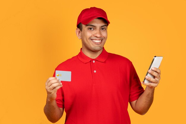 Photo deliveryman using smartphone and credit card on yellow studio background