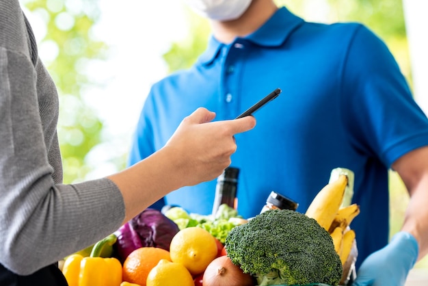 Deliveryman wearing face mask delivering groceries to woman customer that ordered online at home, food delivery service in the times of pandemic cancept