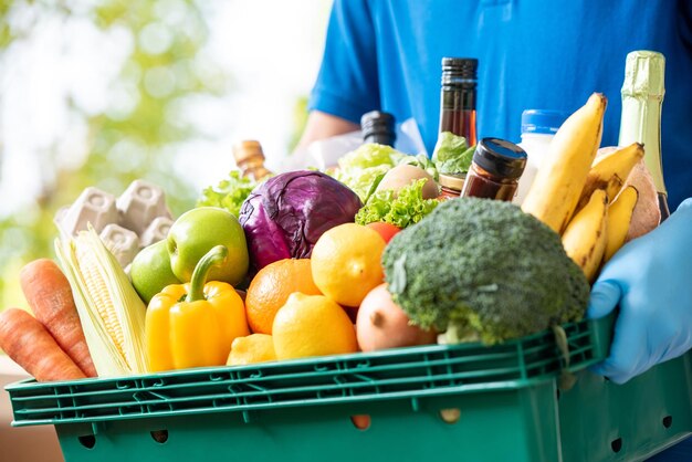 Deliveryman wearing gloves holding grocery basket delivering to\
customer, hygienic food delivery service in the time of pandemic\
concept