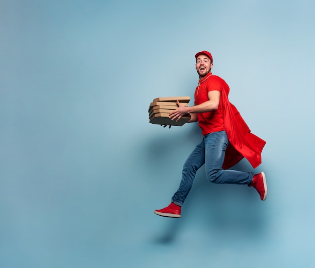 Deliveryman with pizzas acts like a powerful superhero. Concept of success and guarantee on shipment. Studio cyan background