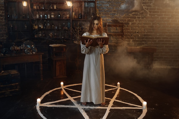 Photo demonic woman with book of spells standing in the magic circle, demons casting out. exorcism, mystery paranormal ritual, dark religion, night horror, potions on shelf