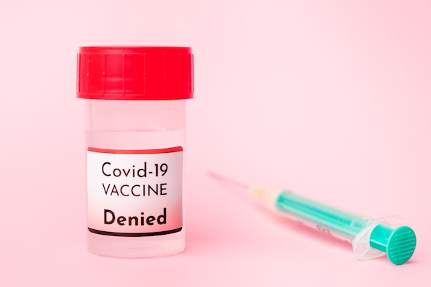 Denied Covid-19 vaccine in the bottle and disposable syringe for injection on the pink background