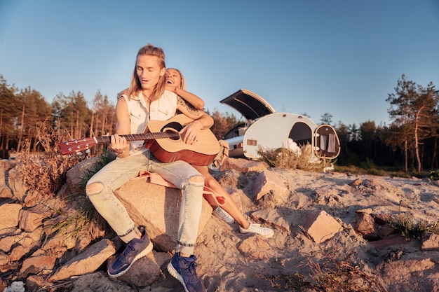 Denim clothes. Handsome athletic man with long blonde hair wearing denim clothes playing the guitar