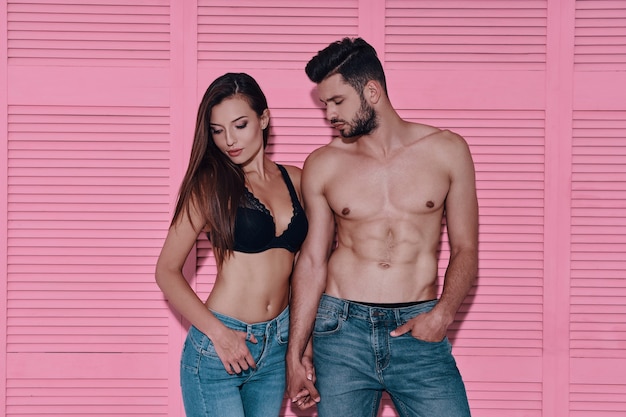 Denim couple. Beautiful young couple holding hands while standing against pink background