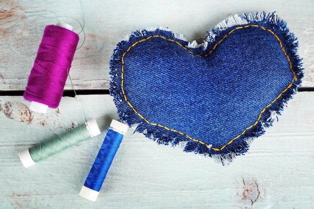 Denim heart and thread on wooden background