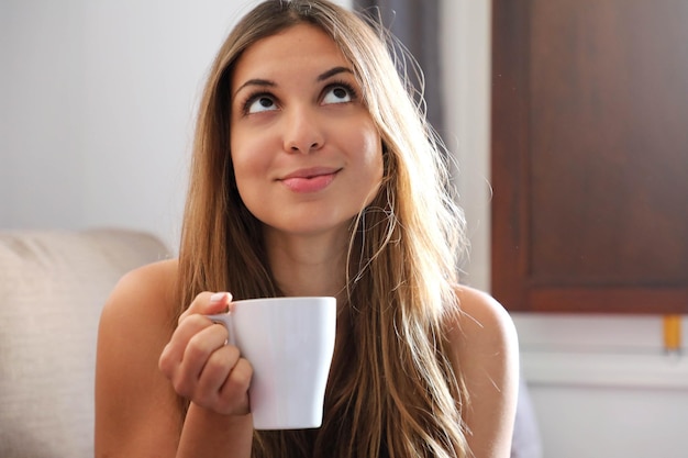 Denken betrokken jonge vrouw opzoeken met kopje koffie op de bank thuis