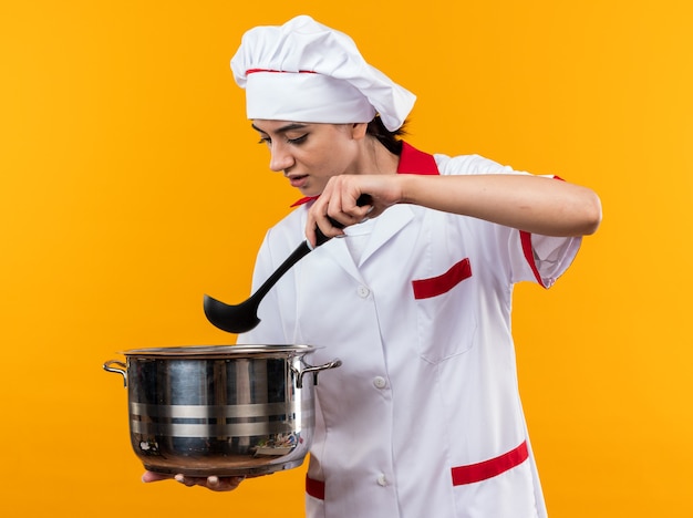 Denkend jong mooi meisje in chef-kok uniform houden en kijken naar steelpan