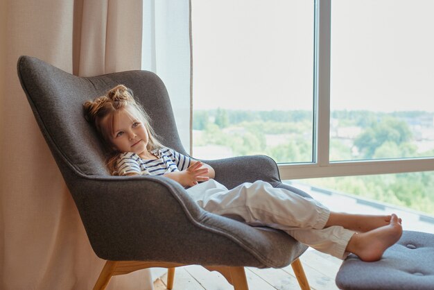 Foto denkend klein schattig meisje zittend op de fauteuil