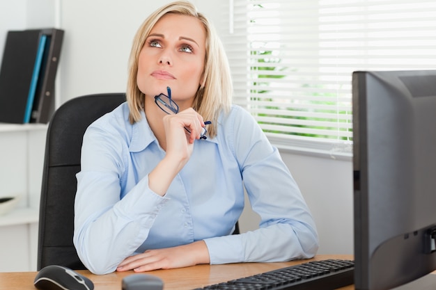 Denkende mooie vrouw achter een bureau die het plafond bekijken