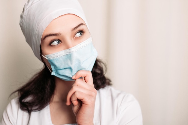 Denkende verpleegster gekleed in medische jurk en gezichtsmasker dragen