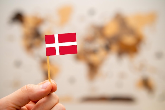 世界地図の背景に男の手でデンマークの旗