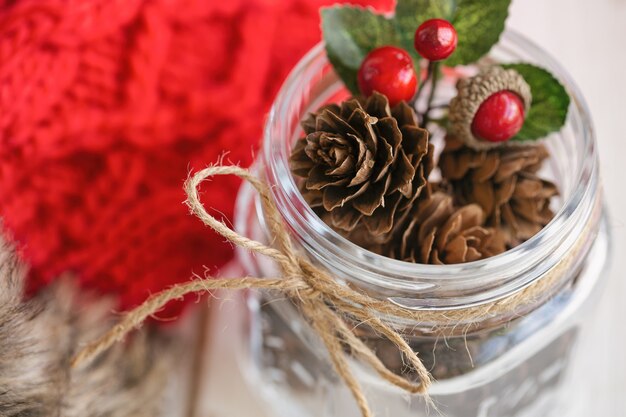 Denneappel of naaldboomkegel en rode hulstballen in glazen fles met rustieke lintvlinderdas. Kerstmisachtergrond met feestelijke de wolhandschoenen van het decoratie rode breigoed voor Kerstmisbehang.