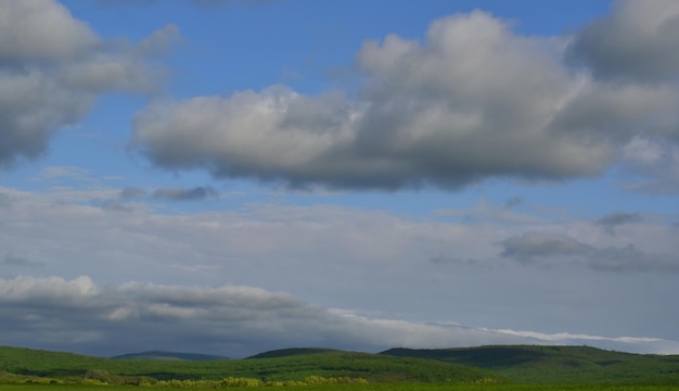 Dense clouds rise above the hills covered with greenerySunny daySpring Krasnodar region Russia