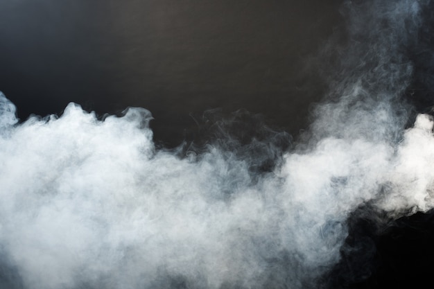 Плотные пушистые клубы белого дыма и тумана на черном фоне, абстрактные облака дыма, движение размыто не в фокусе. Дымящиеся удары от машины сухой лед летят и порхают в воздухе, эффект текстуры