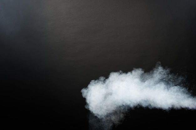 黒の背景に白い煙と霧の濃いふわふわのパフ、抽象的な煙の雲、動きがぼやけて焦点が合っていません。マシンドライアイスフライからのスモーキングブローと空気中の羽ばたき、効果的なテクスチャ