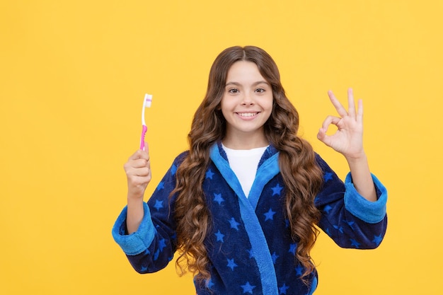 Уход за зубами здоровая красивая улыбка с использованием лучшей зубной пасты детская стоматология хорошо жест девочка-подросток держит зубную щетку счастливый ребенок собирается чистить зубы ребенок в пижаме делает утреннюю рутину