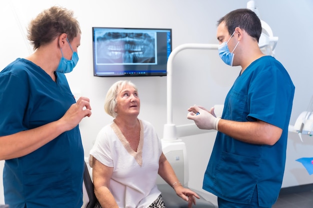 Medico dentista e assistente della clinica odontoiatrica che spiega a una protesi dentaria di trattamento dentale di una donna anziana