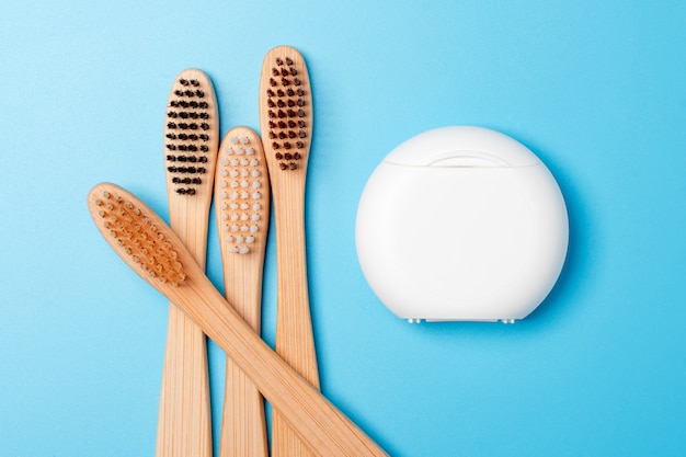 Dental floss container and bamboo toothbrushes on blue background. Daily oral hygiene, teeth care and health. Cleaning products for mouth. Dental care concept.