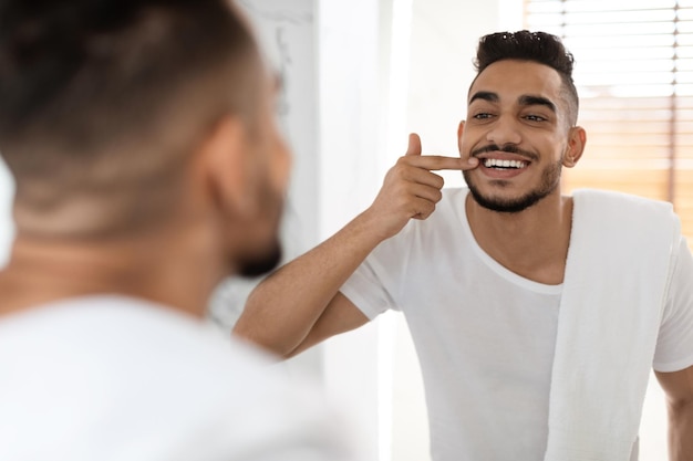 Uomo arabo bello di salute dentale che guarda nello specchio i suoi denti bianchi