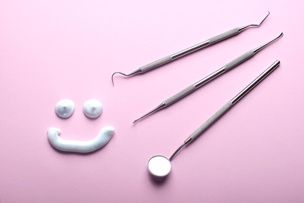 Dental instruments and a smiling toothpaste face on pink background