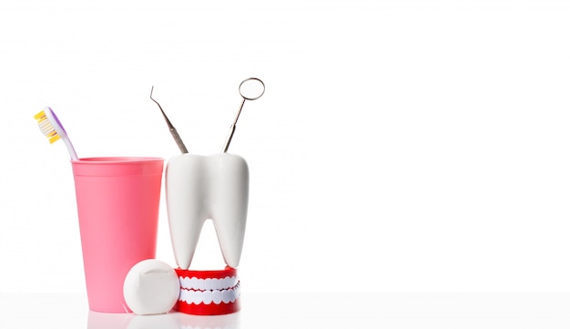 Dental mirror and dental explorer instrument in white tooth model, human jaw and dental floss near toothbrush in pink glass against white isolated background.