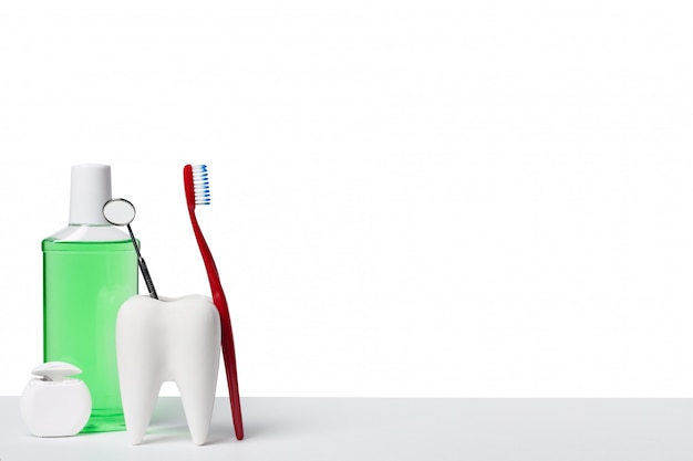 Photo dental mirror in white tooth model near mouthwash, toothbrush and dental floss against white isolated background.