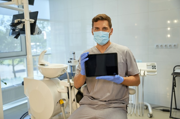 Specialista dentale in maschera e guanti che mostrano lo schermo del tablet