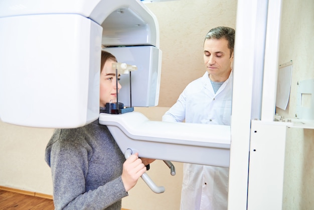 Dental tomography. Girl-patient stands in a tomograph, a doctor near the control panel