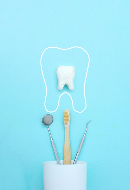 Стоматологическая модель зуба с металлическим медицинским стоматологическим оборудованием инструменты зубы стоматолог рот зеркало зубная щетка в белом стекле уход за зубами на синем фоне с копией пространства крупным планом