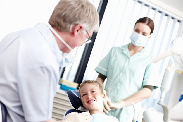 歯科治療クリニックオフィスでアシスタントと歯科医に微笑んでいる少年の肖像画