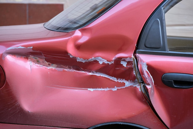 Dented car with damaged body parked on city street side road\
safety and vehicle insurance concept