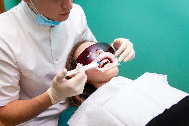 Dentist applies a tooth whitening gel with a syringe. Girl undergoes a teeth whitening procedure in a dental clinic