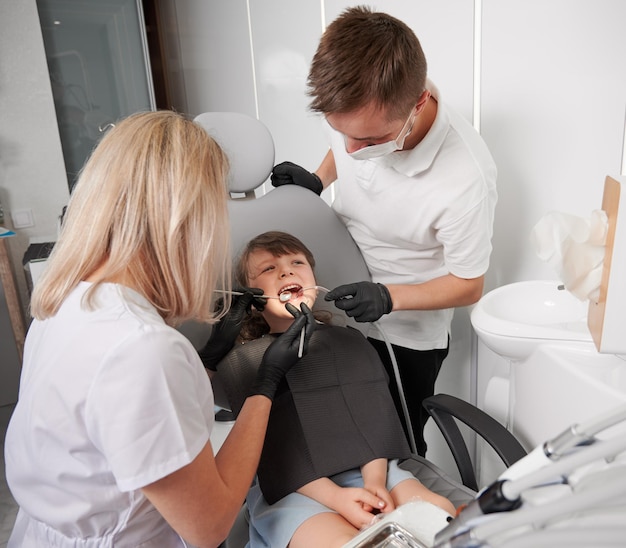 歯科医院で小さな女の子の歯を調べる歯科医と助手
