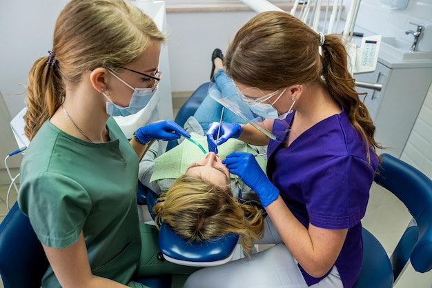 Dentist and assistant in mask treats teeth female patient at the dental office