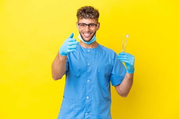 Dentista uomo biondo che tiene gli strumenti isolati sullo sfondo che stringono la mano per chiudere un buon affare